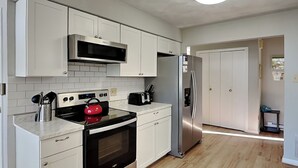 Una cocina moderna con armarios blancos, un microondas de acero inoxidable, una tetera roja, un tostador y un refrigerador.
