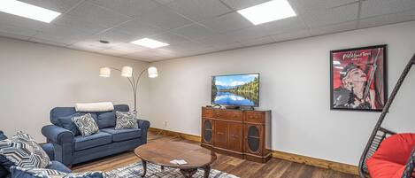 A living room with a blue sofa, a coffee table, a TV on a wooden cabinet, and a poster on the wall.