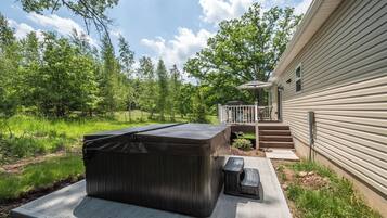 A hot tub and outdoor seating area adjacent to a house with a deck and steps leading to a porch.