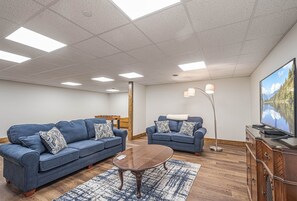 A living room with two blue sofas, a wooden coffee table, a patterned rug, a TV on a wooden cabinet, and a floor lamp. - Happy Ours by Taylor Made Deep Creek (McHenry)