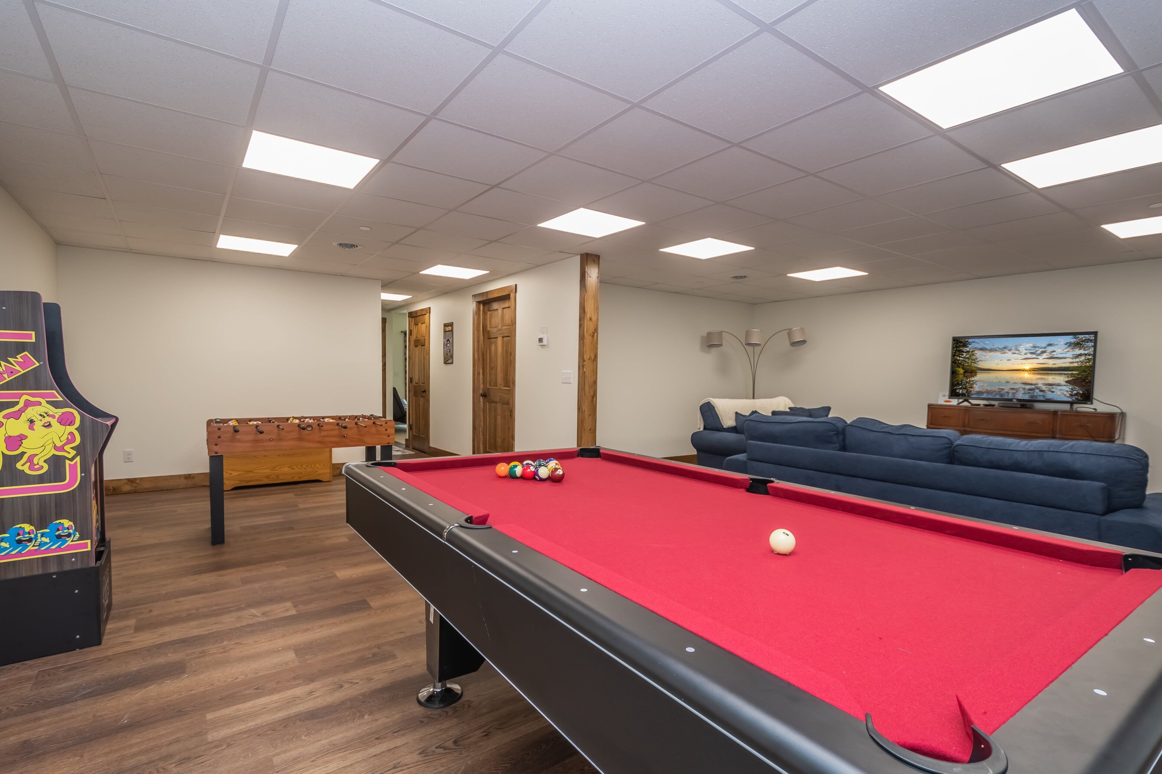 A pool table with balls, a foosball table, a sofa, and a painting on the wall.