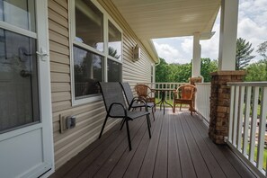 A covered porch with a wooden deck, a table, and two chairs. - Happy Ours by Taylor Made Deep Creek (McHenry)