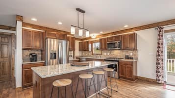 A modern kitchen with wooden cabinets, stainless steel appliances, a granite countertop, and a bar stool area.