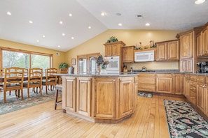 A kitchen with wooden cabinets, a central island, and a dining area with chairs and a table.