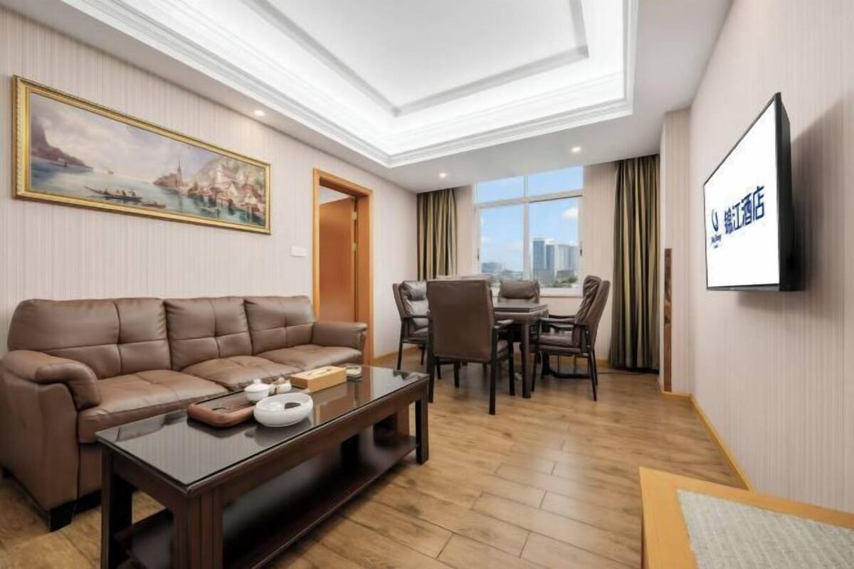 A hotel room with a sofa, coffee table, dining table, chairs, a TV, and a painting on the wall.