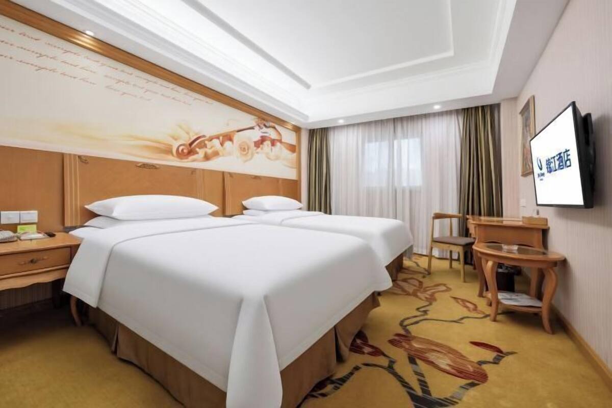 A hotel room with a large bed, a desk, a chair, a television, and a decorative wall.