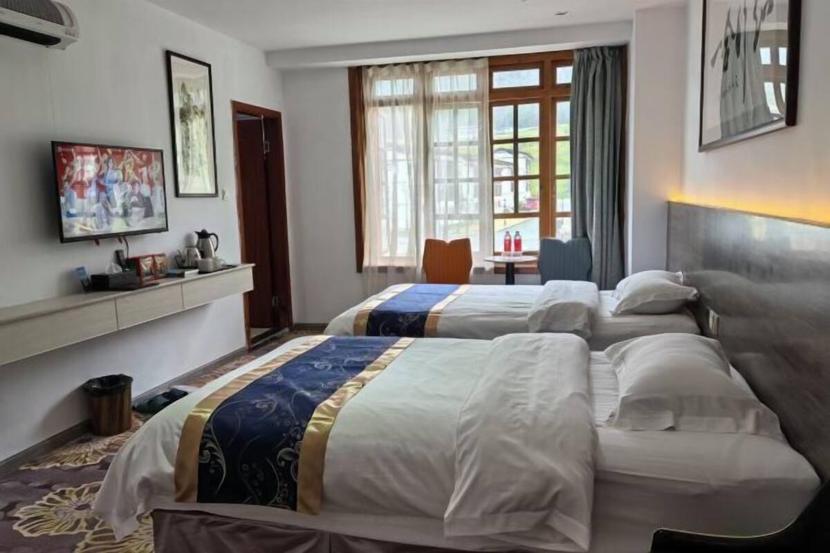 Een hotelkamer met twee bedden, een televisie, een raam met gordijnen en een klein tafeltje met een stoel.