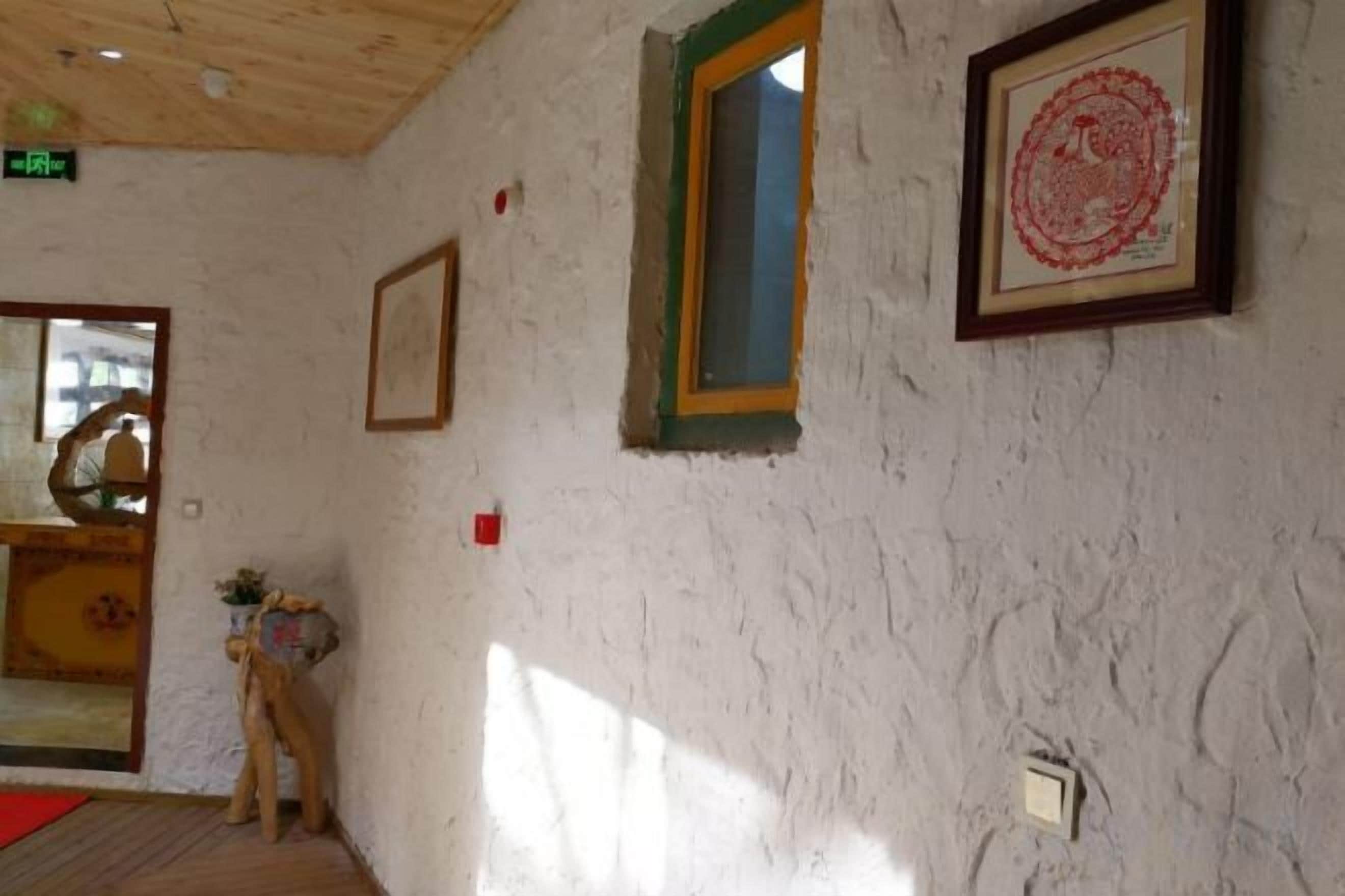 Una habitación con una pared blanca con textura, un cuadro enmarcado, una ventana con marco verde y una puerta con un felpudo rojo.