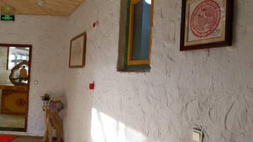 Una habitación con una pared blanca con textura, un cuadro enmarcado, una ventana con marco verde y una puerta con un felpudo rojo.