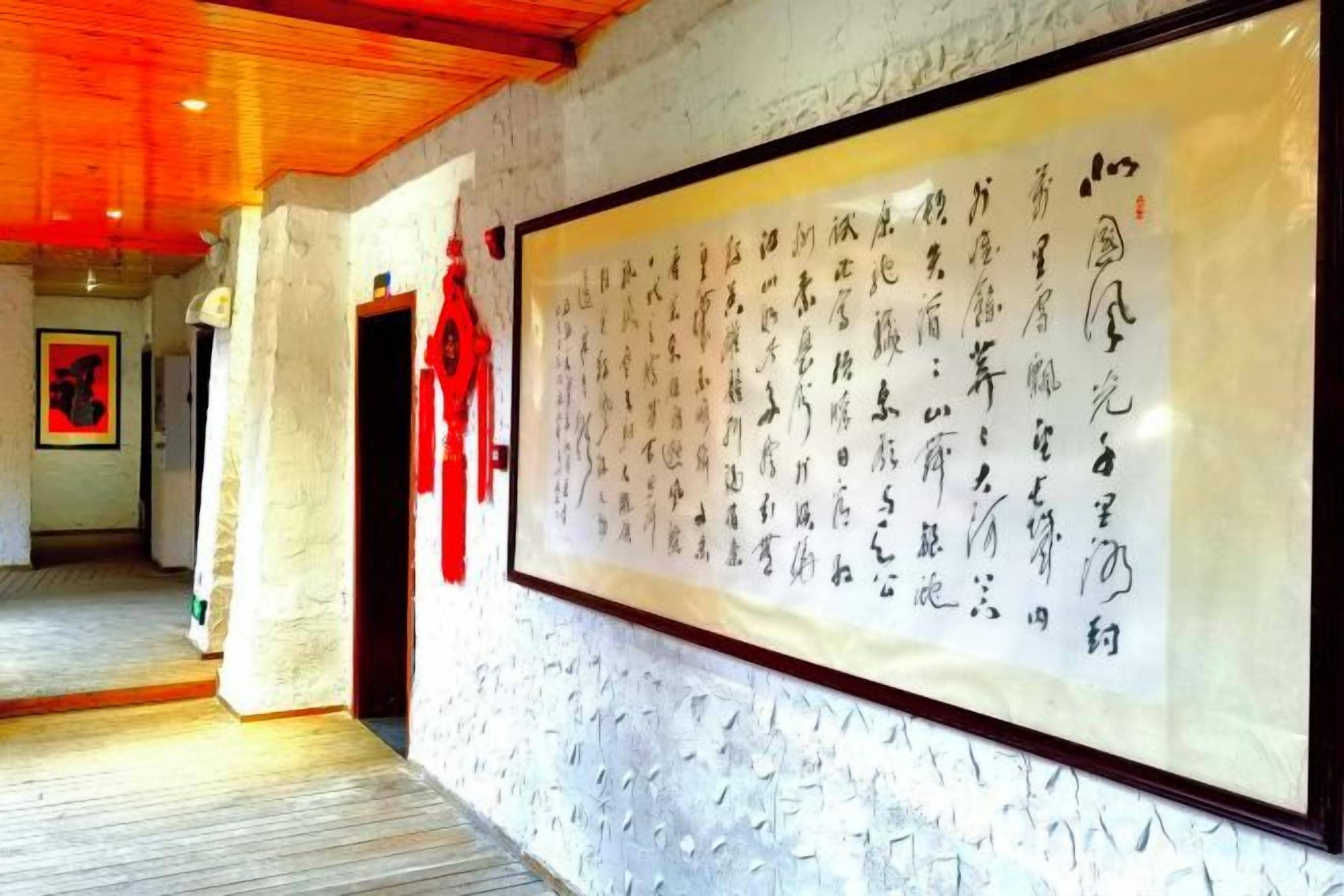 A hallway with a large framed calligraphy artwork on the wall, a wooden ceiling, and a red decorative item hanging on the wall.