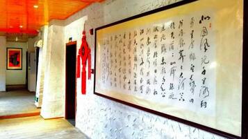 A hallway with a large framed calligraphy artwork on the wall, a wooden ceiling, and a red decorative item hanging on the wall.