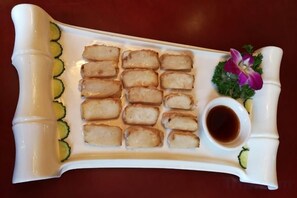 A white rectangular plate with several pieces of food, a small bowl of sauce, and a decorative flower. - Ling Yun Boutique Hotel (Nyingchi)