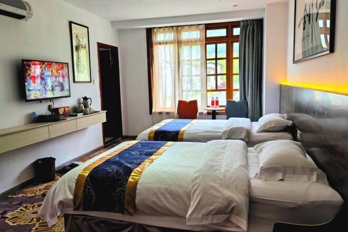 Een hotelkamer met twee bedden, een televisie, een raam met gordijnen en een klein tafeltje met een stoel.