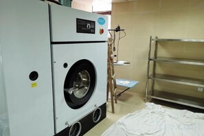 Un lavadero con una lavadora industrial grande, una estantería metálica y una escalera de madera.