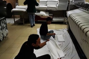 Una habitación con una cama, una mesa con ropa de cama doblada y una persona de pie al fondo.