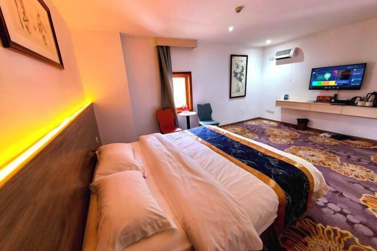 Een hotelkamer met een bed, een bureau, een stoel, een televisie en een airconditioning.