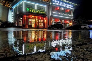 Edificio de dos pisos con letreros iluminados y suelo mojado que refleja la luz.