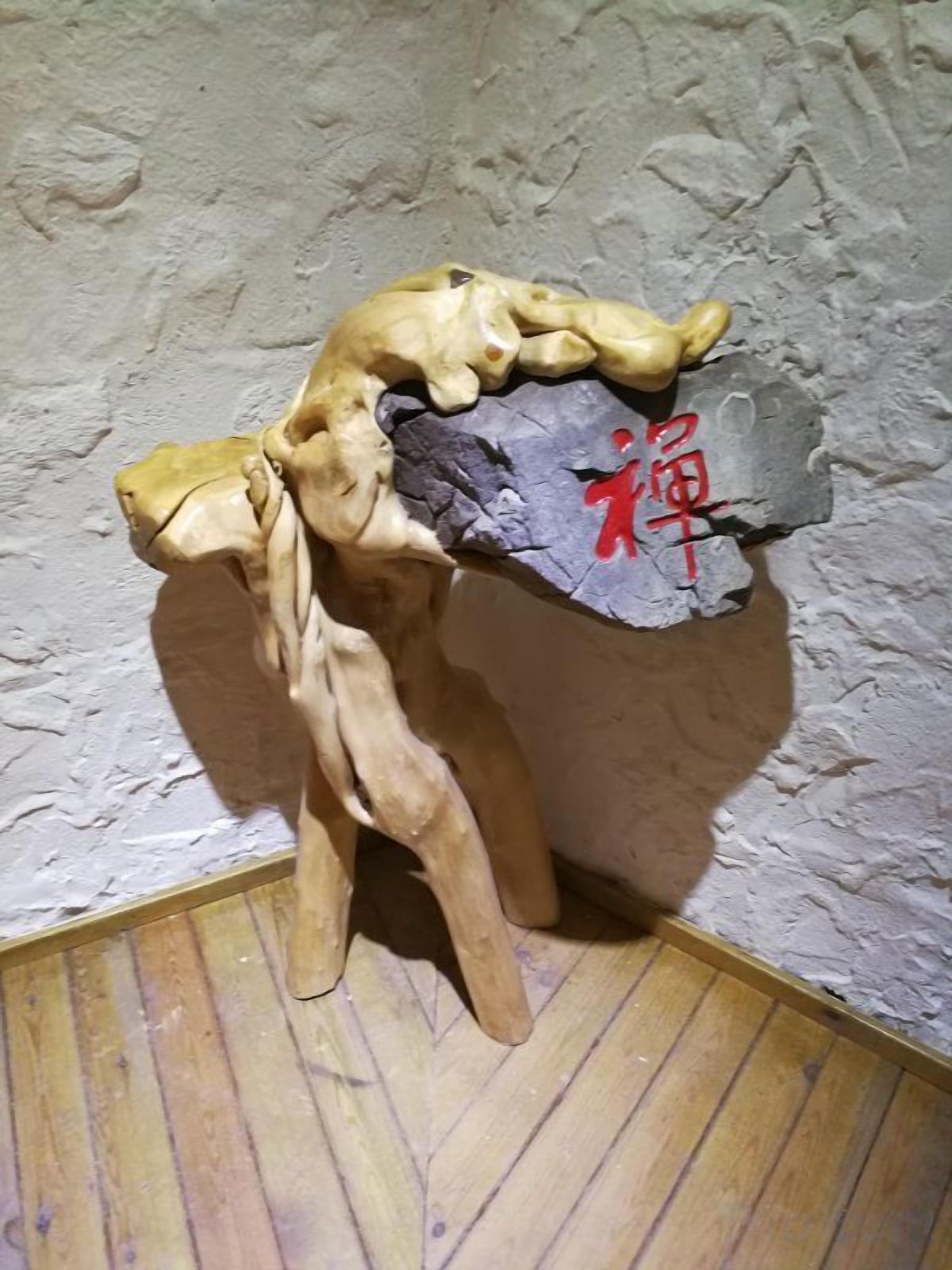 Une sculpture représentant une figure humaine, posée sur un socle en pierre, et placée contre un mur à la texture particulière.