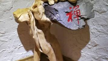 Une sculpture représentant une figure humaine, posée sur un socle en pierre, et placée contre un mur à la texture particulière.
