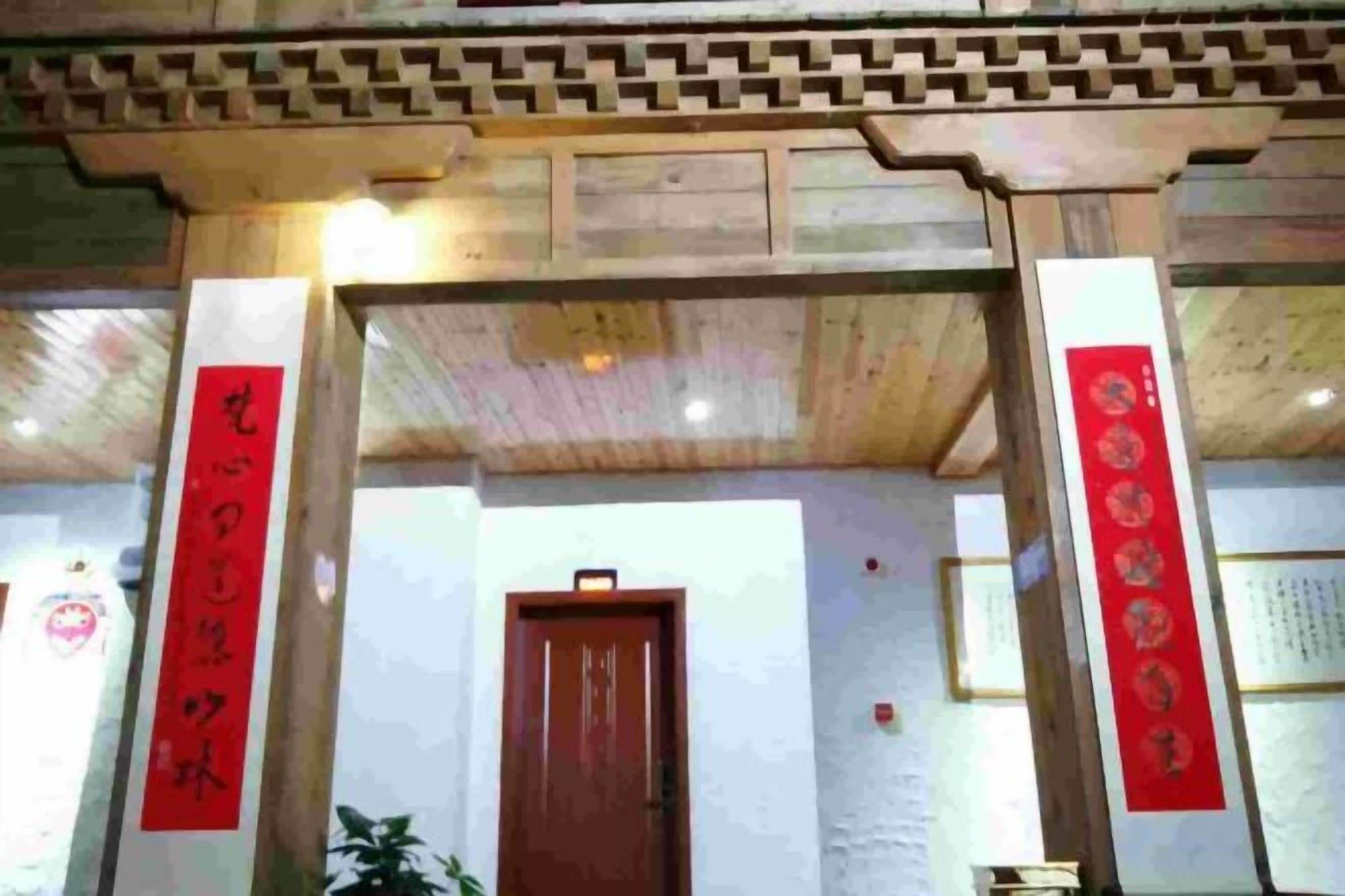Une structure traditionnelle en bois, dotée d’une porte, qui pourrait servir d’espace d’accueil, et ornée de banderoles rouges portant des inscriptions.
