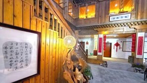 A traditional wooden interior with a framed calligraphy piece, a decorative wooden sculpture, and a staircase leading to an upper level.
