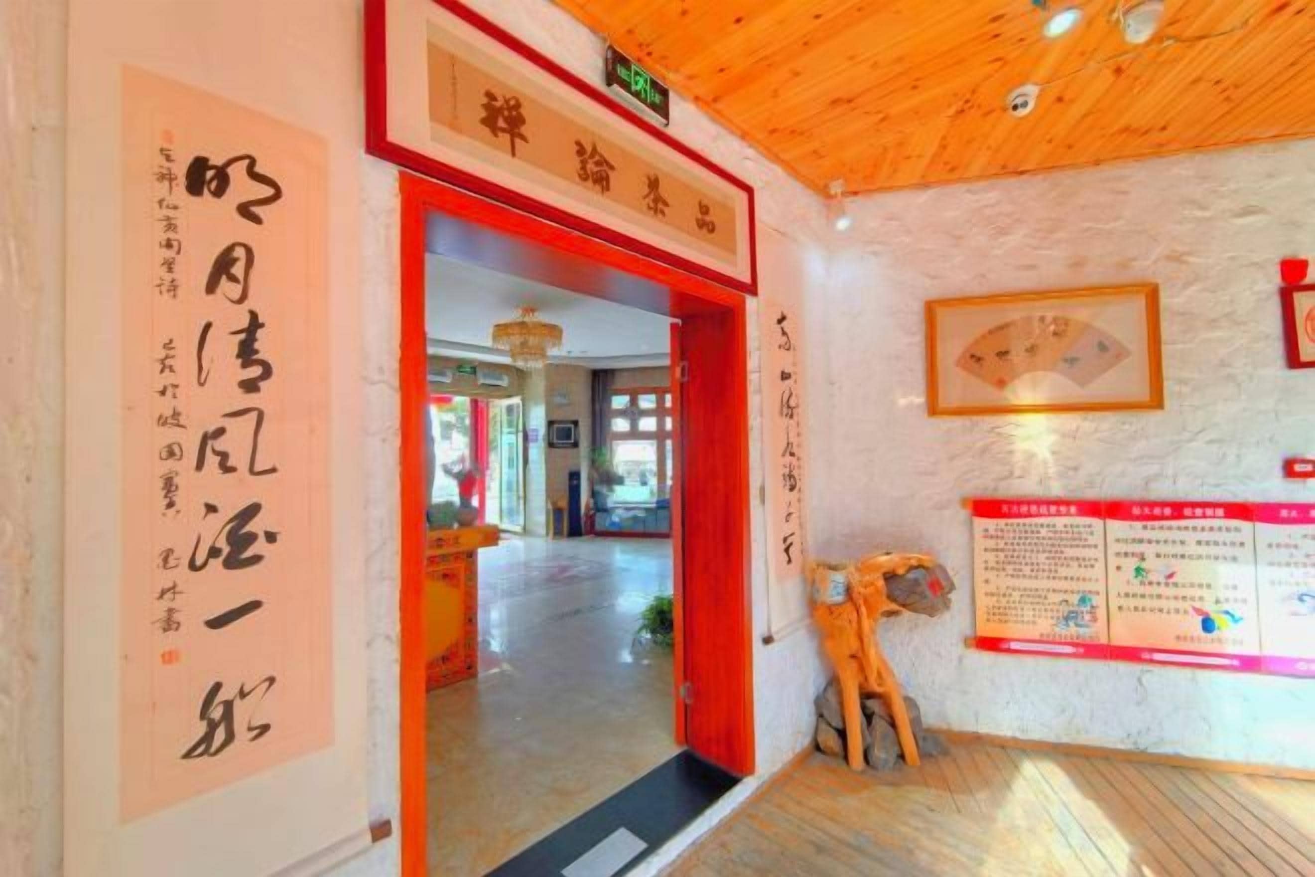 A hotel entrance with a wooden ceiling, a red door, and a wall with informational posters.