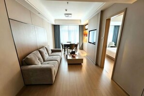 A modern hotel room with a sofa, a dining table, and a TV.