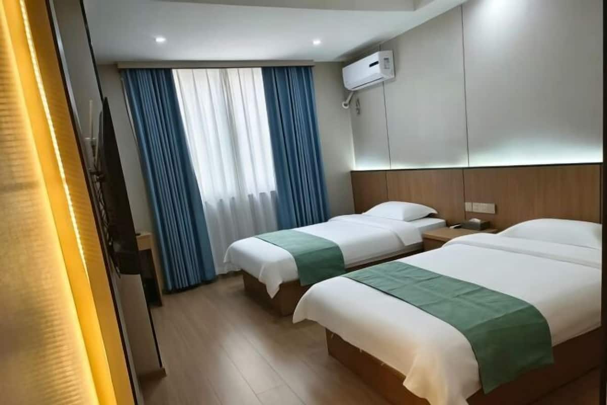 Een hotelkamer met twee bedden, een raam met gordijnen, een airconditioning en een houten hoofdbord.