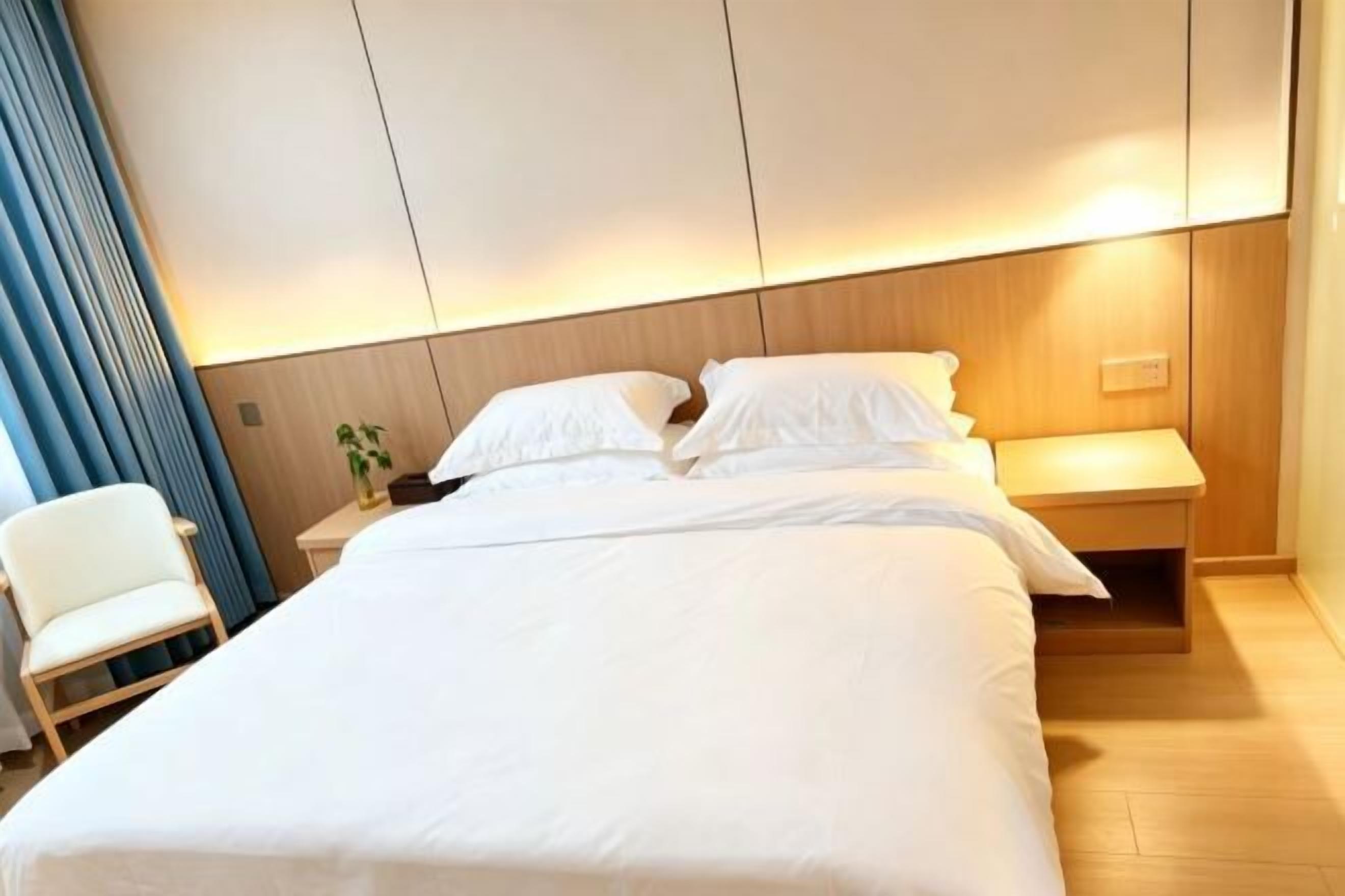 A hotel room with a large bed, a bedside table, a chair, and a wall-mounted light.
