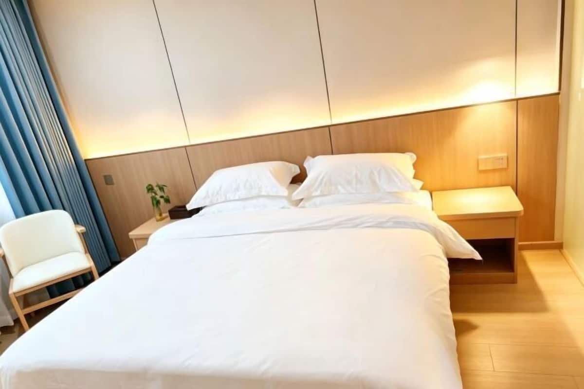 Een hotelkamer met een groot bed, een nachtkastje, een stoel en een wandlamp.