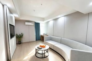 Ett modernt vardagsrum med en böjd soffa, ett runt soffbord, en platt-TV och ett litet sidobord.