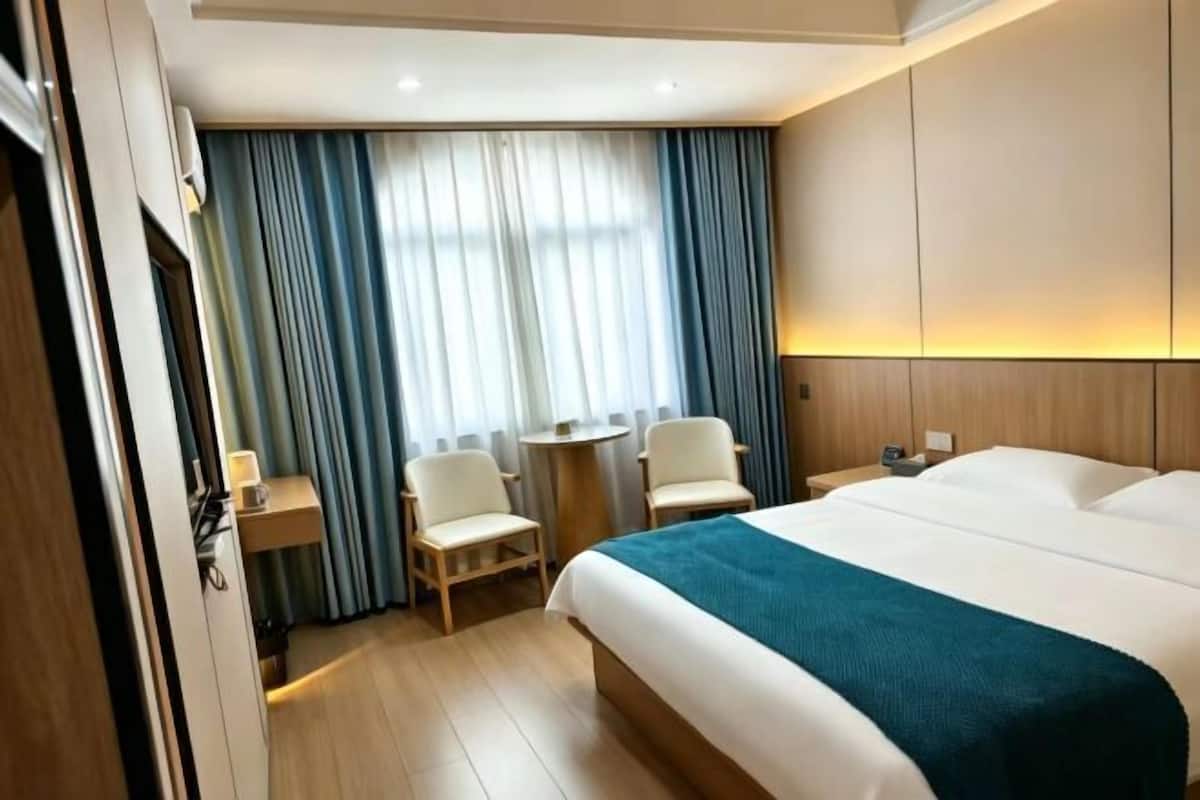 Een hotelkamer met een groot bed, twee stoelen, een tafeltje en een raam met gordijnen.
