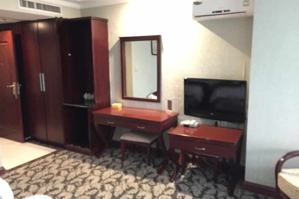 Una habitación de hotel con un armario de madera, un escritorio con una silla, un televisor y una alfombra estampada.