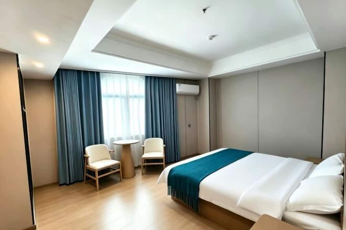 Een hotelkamer met een bed, twee stoelen, een tafeltje en een raam met gordijnen.