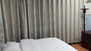 A neatly made bed with a white bedspread and pillows, a wooden nightstand with a lamp, and a patterned curtain in the background. - Hotels Hua Feng (Shangrao)