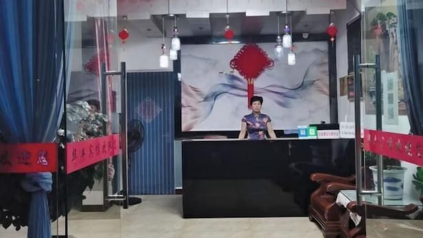 A reception area with a receptionist, a large screen, and red decorations. - Hotels Hua Feng (Shangrao)