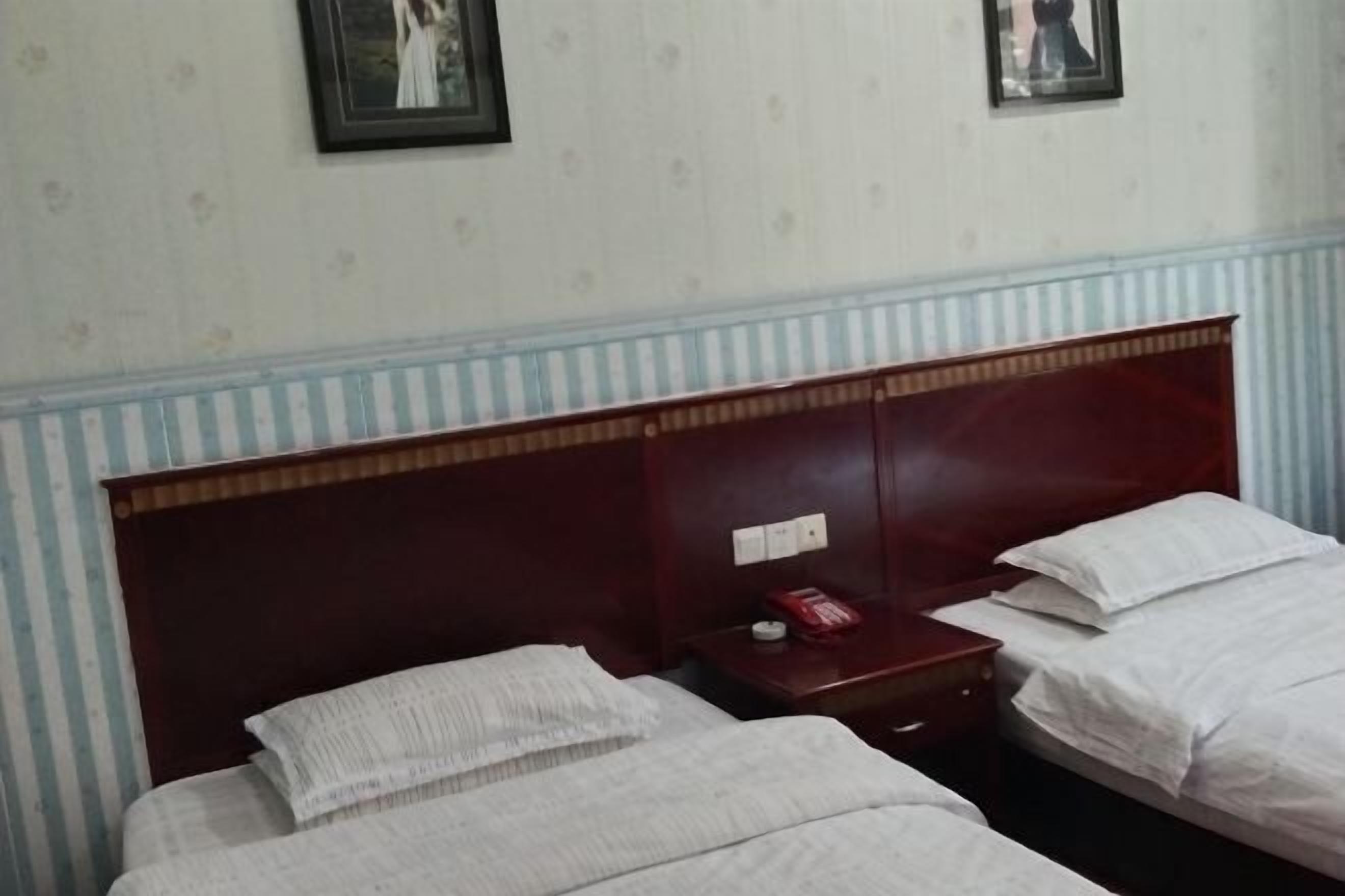 A hotel room with two beds, a wooden headboard, a nightstand with a telephone, and a wall with framed pictures.