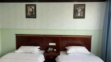 Ein Hotelzimmer mit zwei Einzelbetten, einem Holzkopfende, einem Nachttisch mit Telefon und Lampe sowie zwei gerahmten Bildern an der Wand.