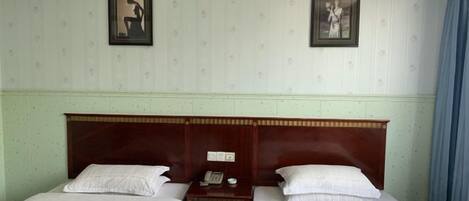 Een hotelkamer met twee enkele bedden, een houten hoofdbord, een nachtkastje met telefoon en lamp, en twee ingelijste foto's aan de muur.
