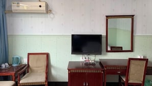 A hotel room with a bed, a desk with a chair, a television, a mirror, and an air conditioning unit. - Hotels Hua Feng (Shangrao)
