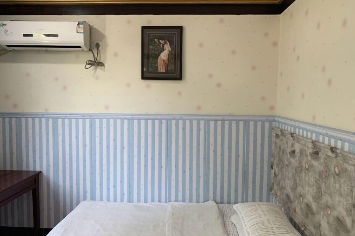 Quarto com cama, papel de parede listrado, quadro na parede e um aparelho de ar condicionado.