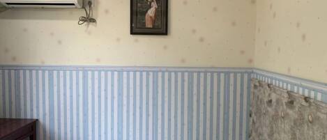 Ein Zimmer mit einem Bett, Streifenmuster-Tapete, einem gerahmten Bild an der Wand und einer Klimaanlage.