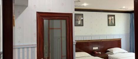 A hotel room with two single beds, a wooden headboard, a small bedside table, and a door with a glass panel.