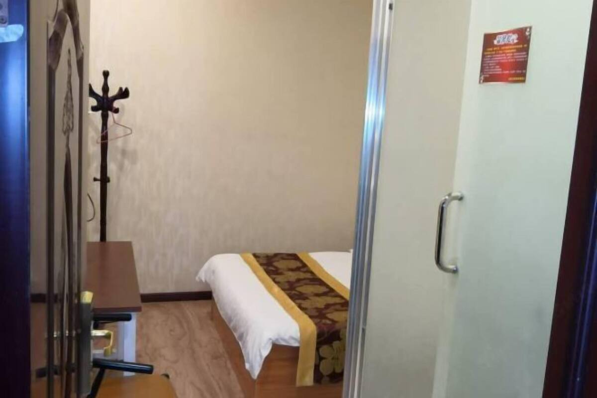 Una habitación de hotel con una cama, un perchero y una puerta con picaporte.