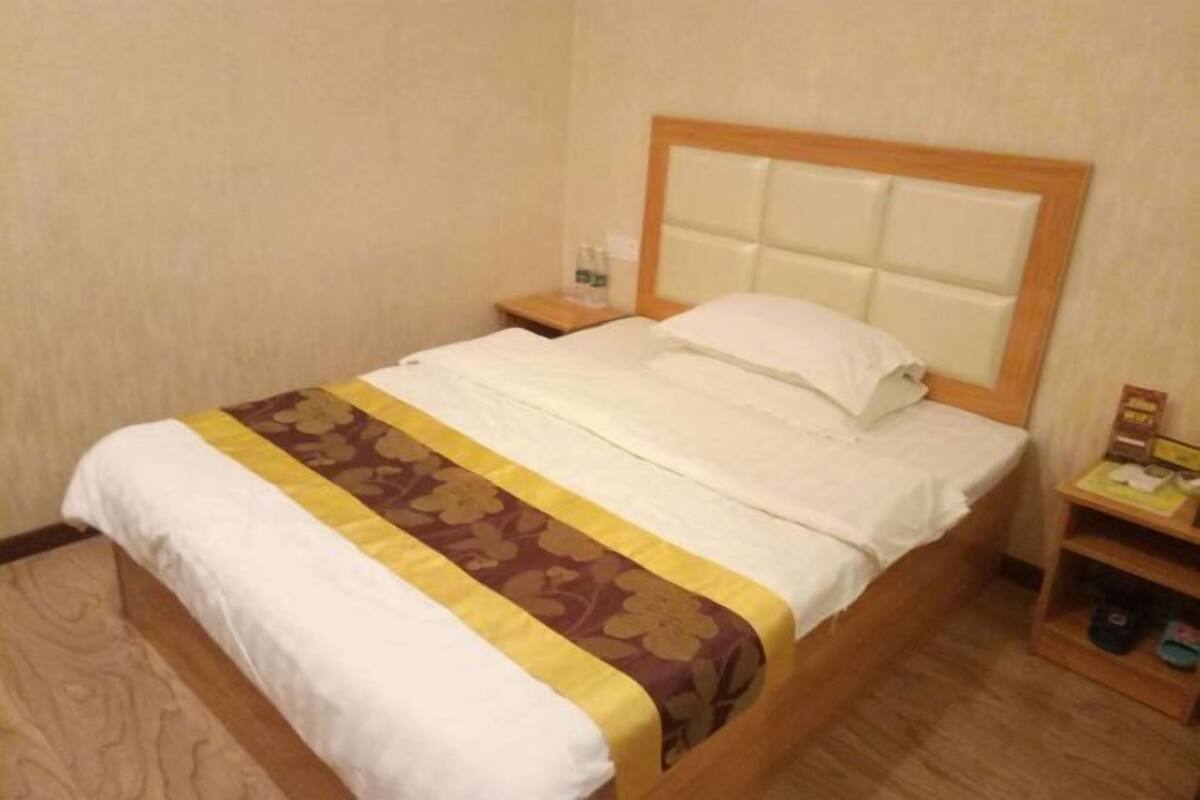 Habitación de hotel con una cama, una mesita de noche y un pequeño estante de madera con un par de zapatillas.