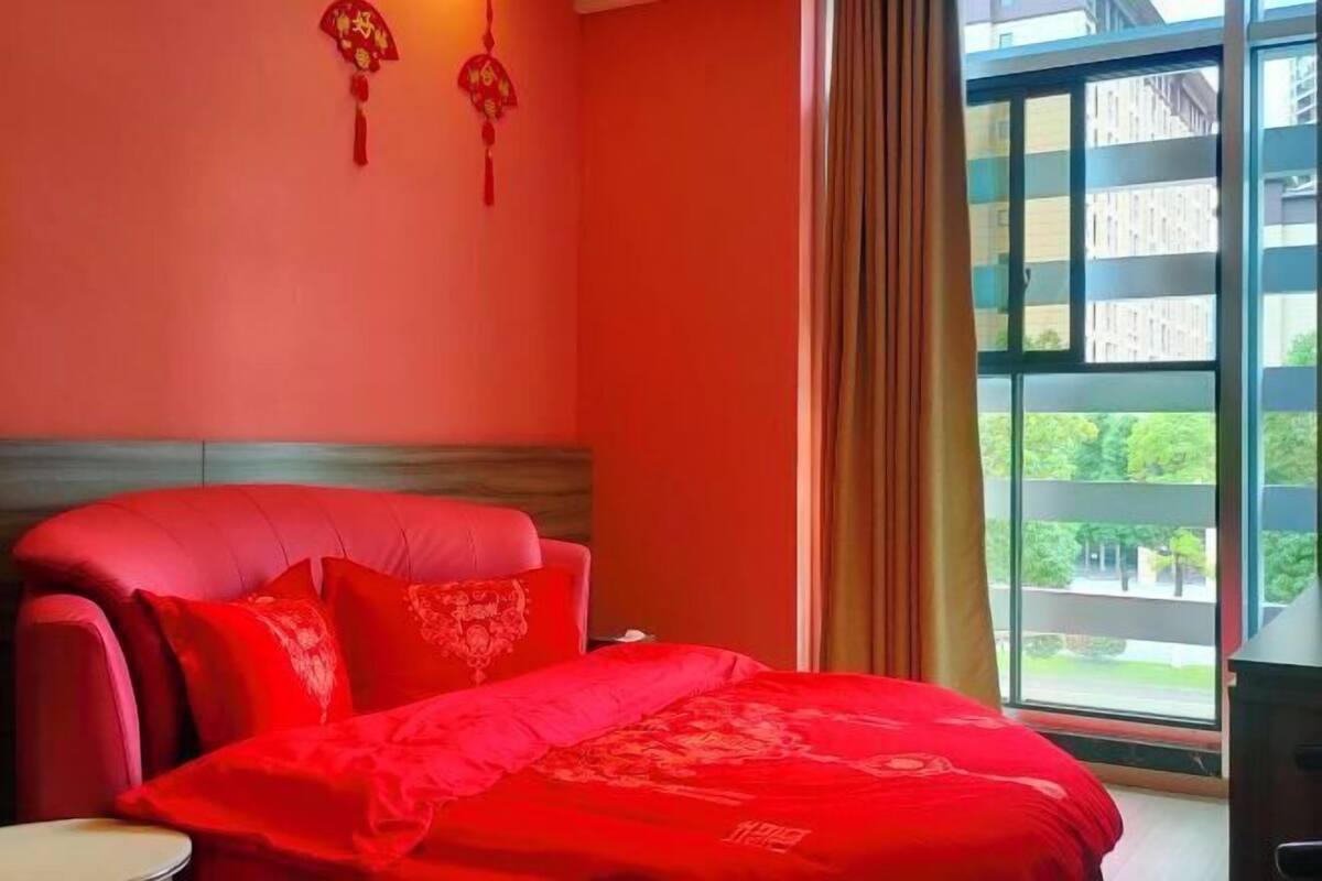 Habitación de hotel con una cama grande, ventana con cortinas y vistas a edificios.
