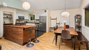 Une cuisine moderne avec des meubles blancs, un îlot central et un coin repas comprenant une table et des chaises en bois.