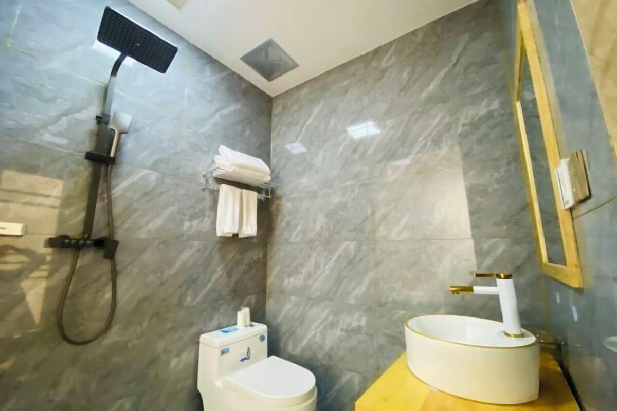 A bathroom with a marble wall, a shower, a toilet, and a sink with a gold faucet.