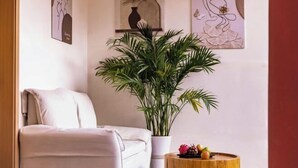 Una habitación con un sofá blanco, una planta grande en maceta y una mesita de madera con frutas.