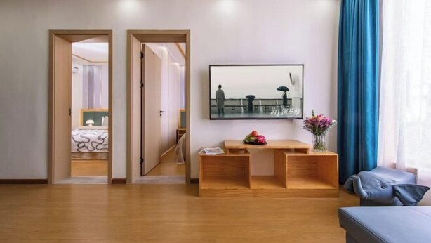 Una sala moderna con un banco de madera, un televisor de pantalla plana montado en la pared y un amplio ventanal con cortinas azules.